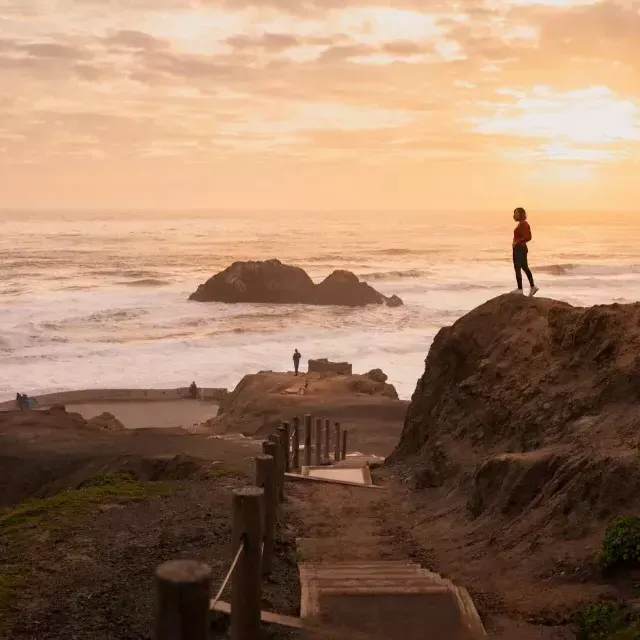 Zwei Menschen stehen auf Felsen mit Blick auf den Ozean bei den Sutro Baths in San Francisco.